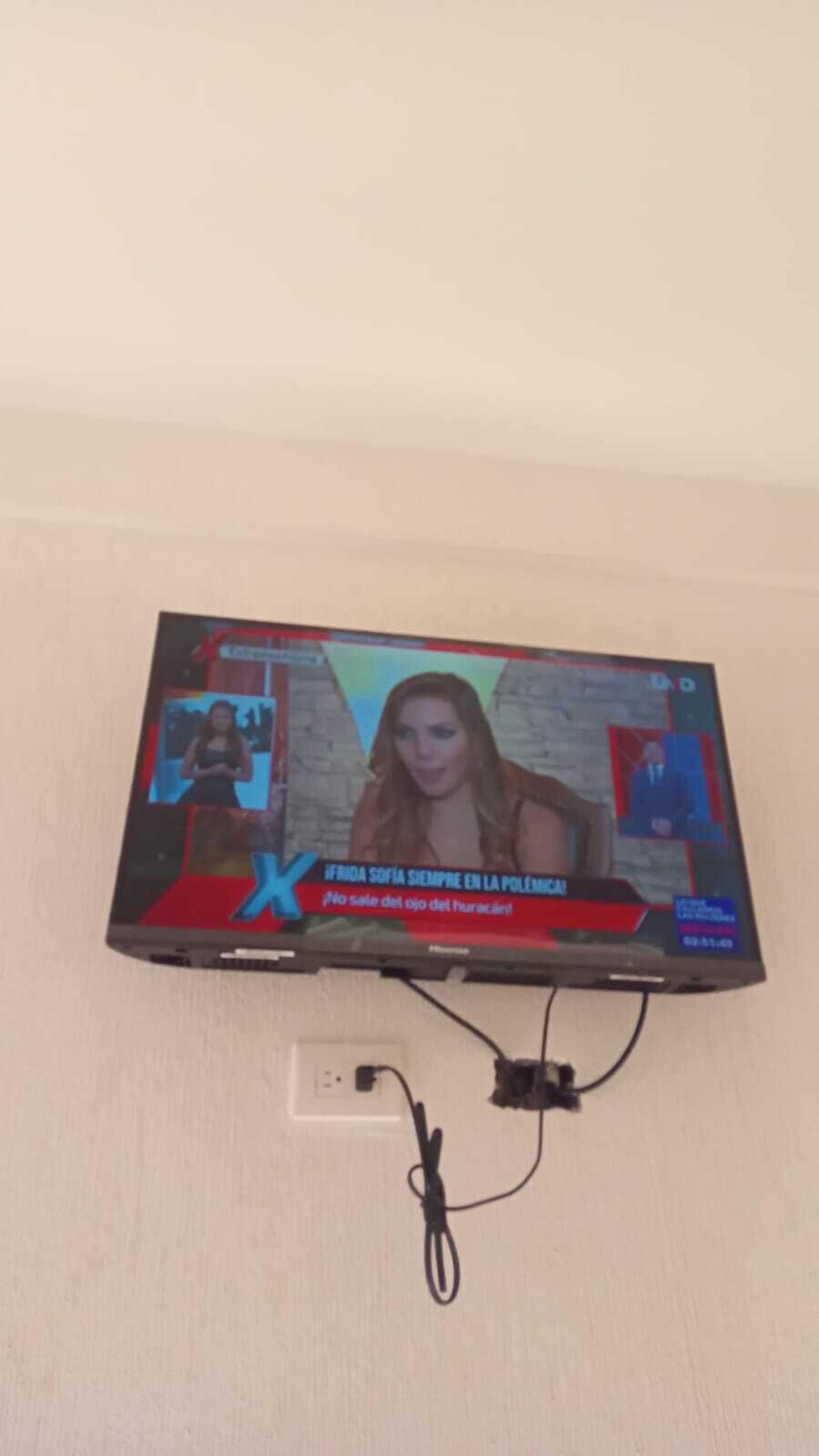 A television mounted on a wall displaying a news broadcast.
