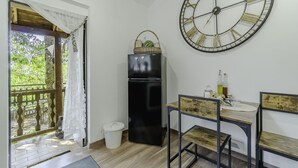Een compacte keuken met een zwarte koelkast, een grote wandklok en een eethoek met houten stoelen en een kleine tafel.