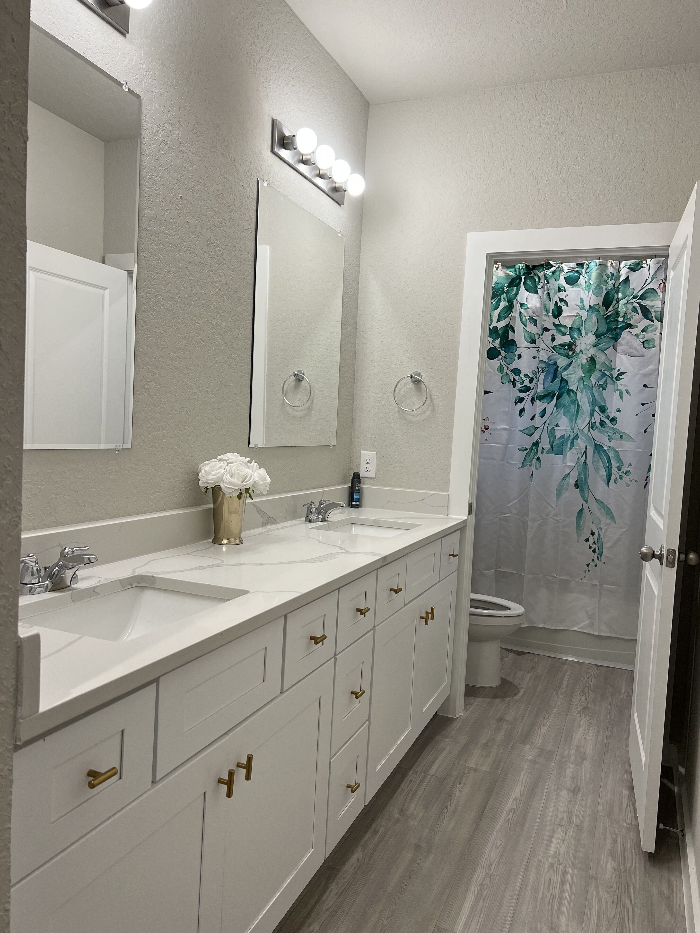 Une salle de bain moderne avec un meuble-lavabo à deux vasques, un grand miroir et un rideau de douche orné de motifs floraux.