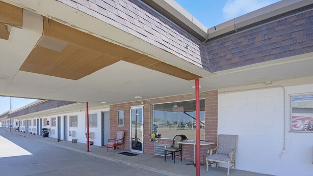 A motel with a covered outdoor seating area, individual rooms, and a brick facade. - First Inn By OYO Quinter Hwy 70 (Quinter)