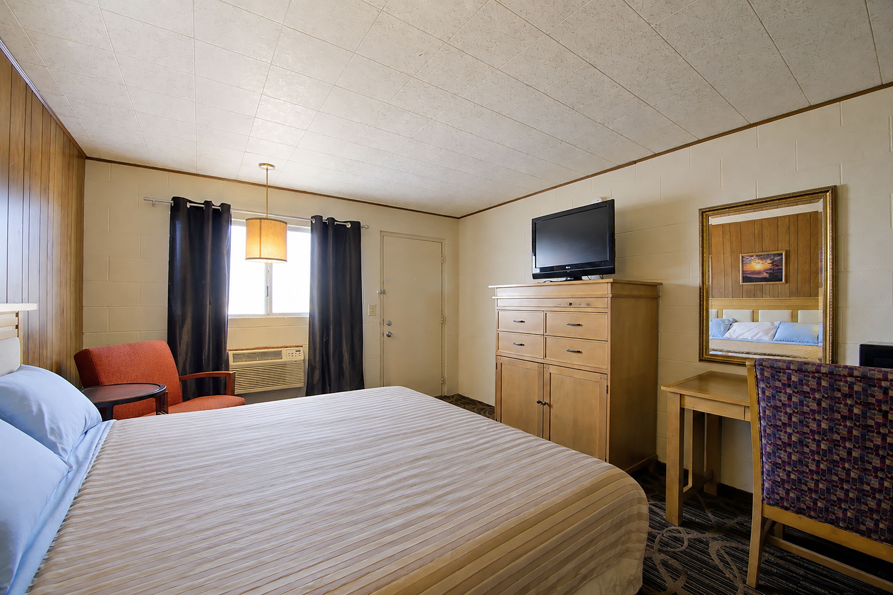 Quarto de hotel com cama, televisão, escrivaninha, cadeira e janela com cortinas.