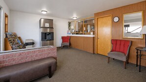 A compact hotel room with a kitchenette, a seating area with a bench, a small table, and a mirror. - First Inn By OYO Quinter Hwy 70 (Quinter)