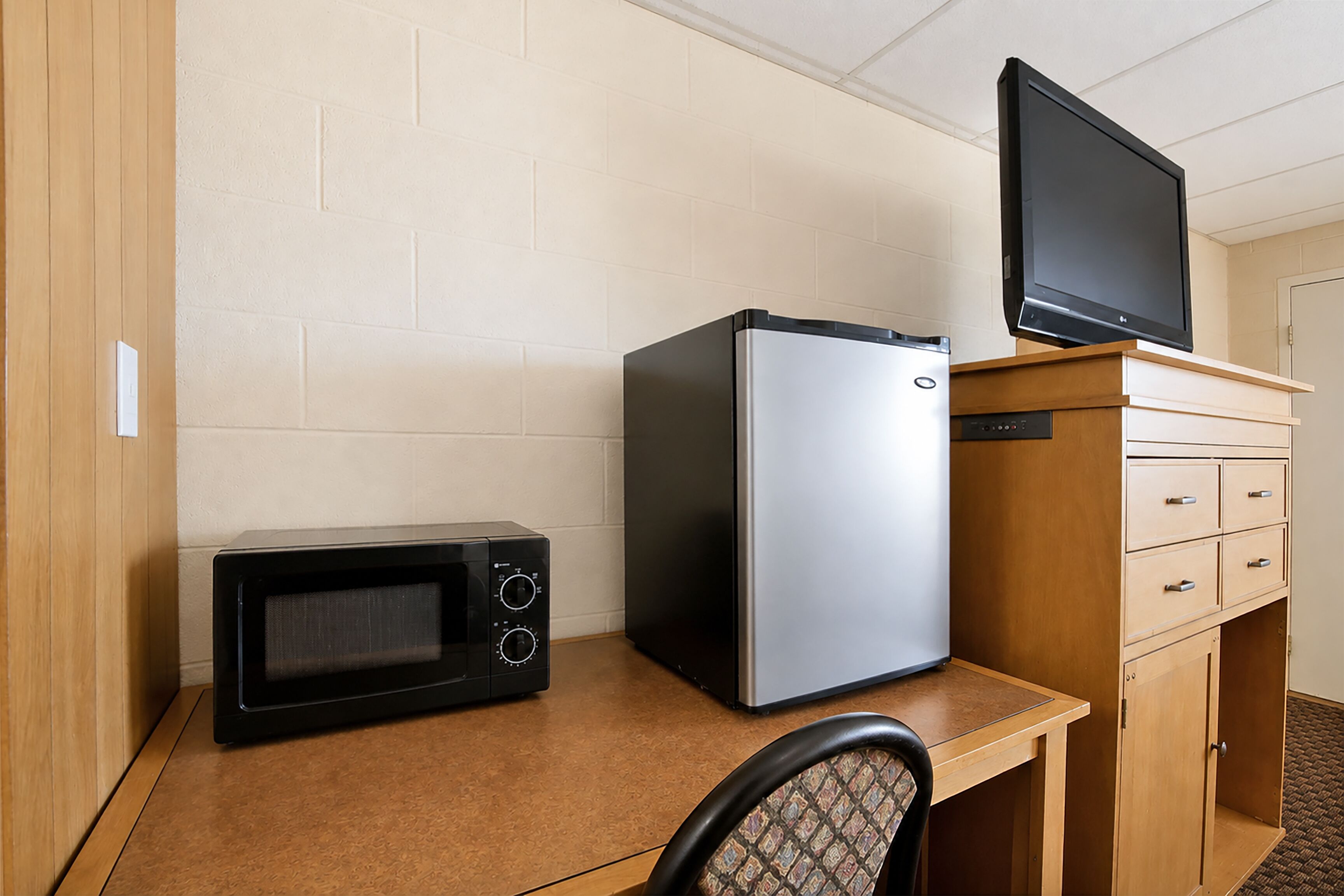 Una kitchenette con microondas, refrigerador y televisor sobre un mueble de madera.