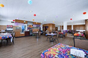 A restaurant with wooden floors, tables with colorful tablecloths, and hanging decorations. - First Inn By OYO Quinter Hwy 70 (Quinter)