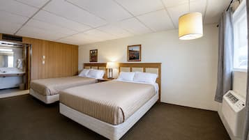 Habitación de hotel con dos camas, cabecero de madera, ventana con cortinas, calentador de pared y una mesita con lámpara.