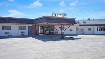 Un motel avec un panneau indicateur, une entrée abritée et un parking en gravier.