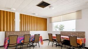 A conference room with a long table, six chairs, and a window with a view of trees. - First Inn By OYO Quinter Hwy 70 (Quinter)