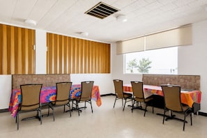 A conference room with a long table, six chairs, and a window with a view of trees. - First Inn By OYO Quinter Hwy 70 (Quinter)