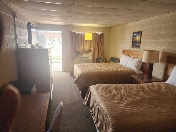 A hotel room with two beds, a desk, a chair, and a television. - First Inn By OYO Quinter Hwy 70 (Quinter)