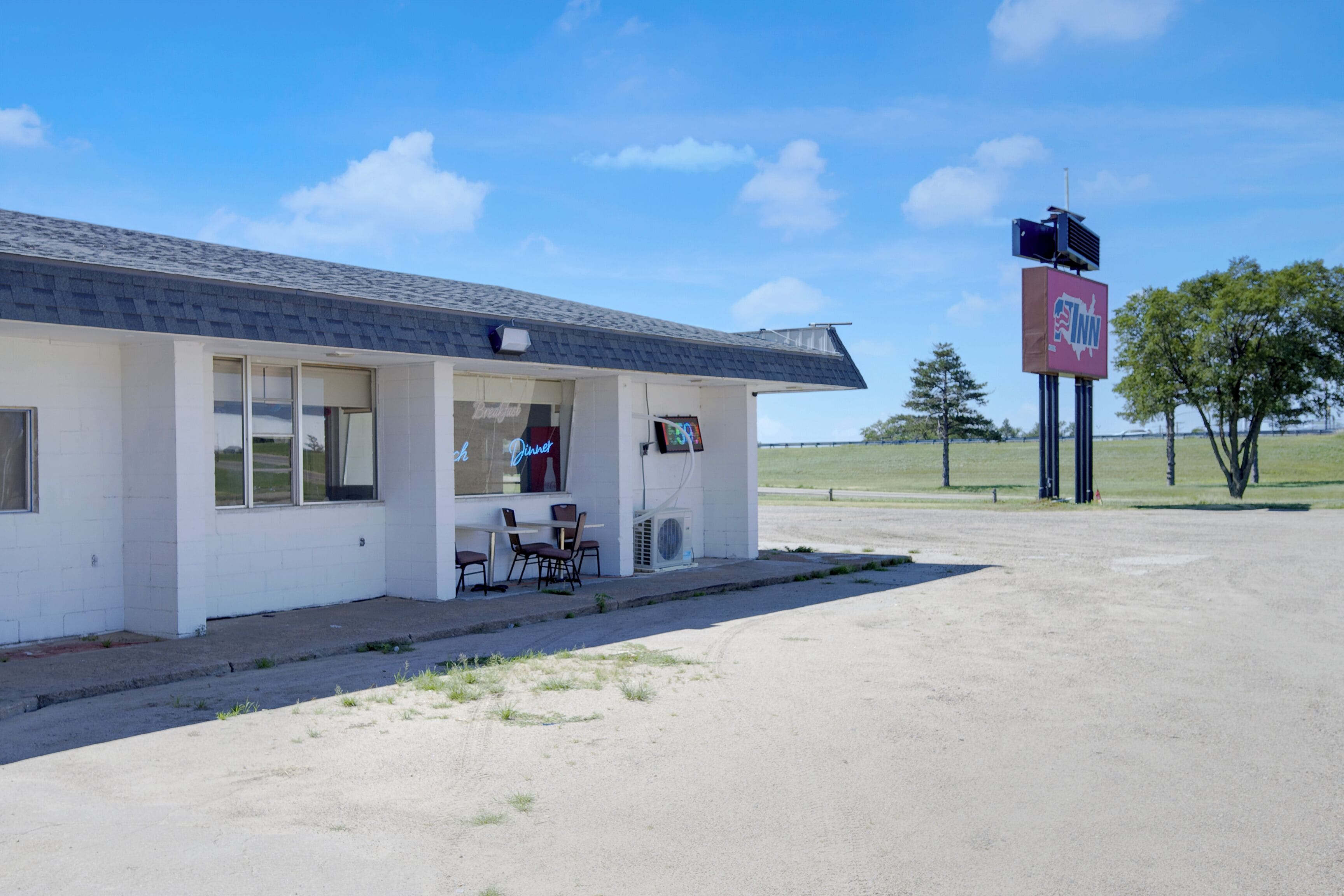 A small building with a signboard, a table, and chairs outside.
