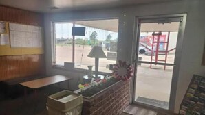 A room with a window, a trash bin, a small table, and a door leading outside. - First Inn By OYO Quinter Hwy 70 (Quinter)