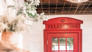 A red telephone booth with a crown emblem, a wooden shelf with jars, and a wicker chair. - Pickleball Cafe & Micro Hotel (Ironton)