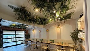 A restaurant interior with wooden tables and chairs, green cushioned benches, and a ceiling adorned with hanging plants and lights. - Pickleball Cafe & Micro Hotel (Ironton)