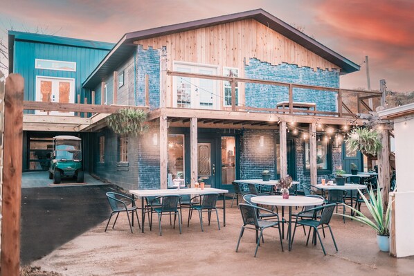 A two-story building with a wooden exterior and blue accents, featuring outdoor seating and a covered patio area.