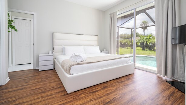 A bedroom with a large bed, a nightstand, a TV, and a sliding glass door leading to a pool. - Pristine Fully Renovated House - 12min from Disney Parks (Kissimmee)