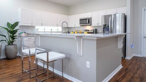 A modern kitchen with white cabinets, stainless steel appliances, and a central island with bar stools. - Pristine Fully Renovated House - 12min from Disney Parks (Kissimmee)