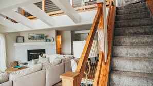 Una sala de estar moderna con una escalera, chimenea y un techo alto con tragaluces.