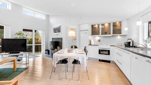 Una cocina moderna con armarios blancos, una zona de comedor con mesa y sillas, y un televisor en la sala de estar.