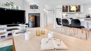Una sala de estar moderna con un televisor de pantalla plana, una chimenea, un comedor con sillas y una mesa, y una cocina con armarios y una lámpara colgante.