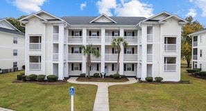 A multi-story residential building with balconies, a central walkway, and a parking sign.