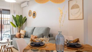 A modern living room with a grey sofa, a dining table set with plates, glasses, and a vase. There is a large plant and a hanging light fixture above the table. - Beautiful apartment on the beach (Torrevieja)