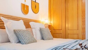 A neatly made bed with white and patterned pillows, a wooden headboard, and a nightstand with a lamp. - Beautiful apartment on the beach (Torrevieja)