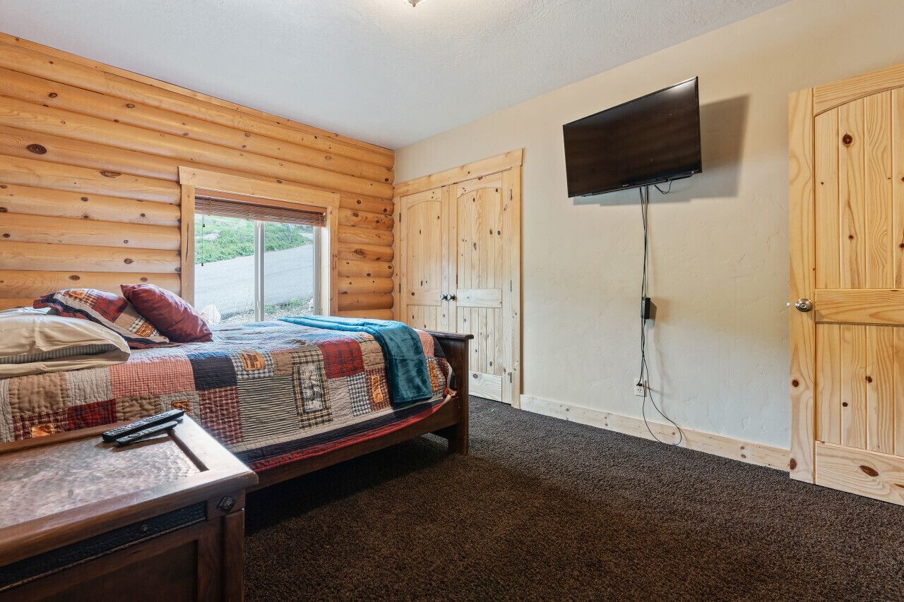 Ein Schlafzimmer mit einer Wand aus Holzstämmen, einem Bett mit einer Steudecke, einem an der Wand montierten Fernseher und einer Holztür.