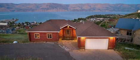 A log cabin with a garage, surrounded by a scenic view of mountains and a lake.