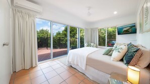 A bedroom with a large bed, a nightstand, a lamp, and a view of the outdoors through a sliding glass door. - Seascape on Shutehaven (Shute Harbour)