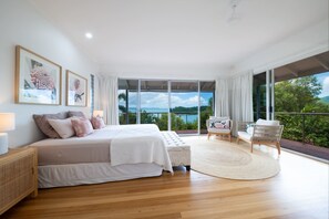 A spacious bedroom with a large bed, a balcony with wicker furniture, and a view of the outdoors.