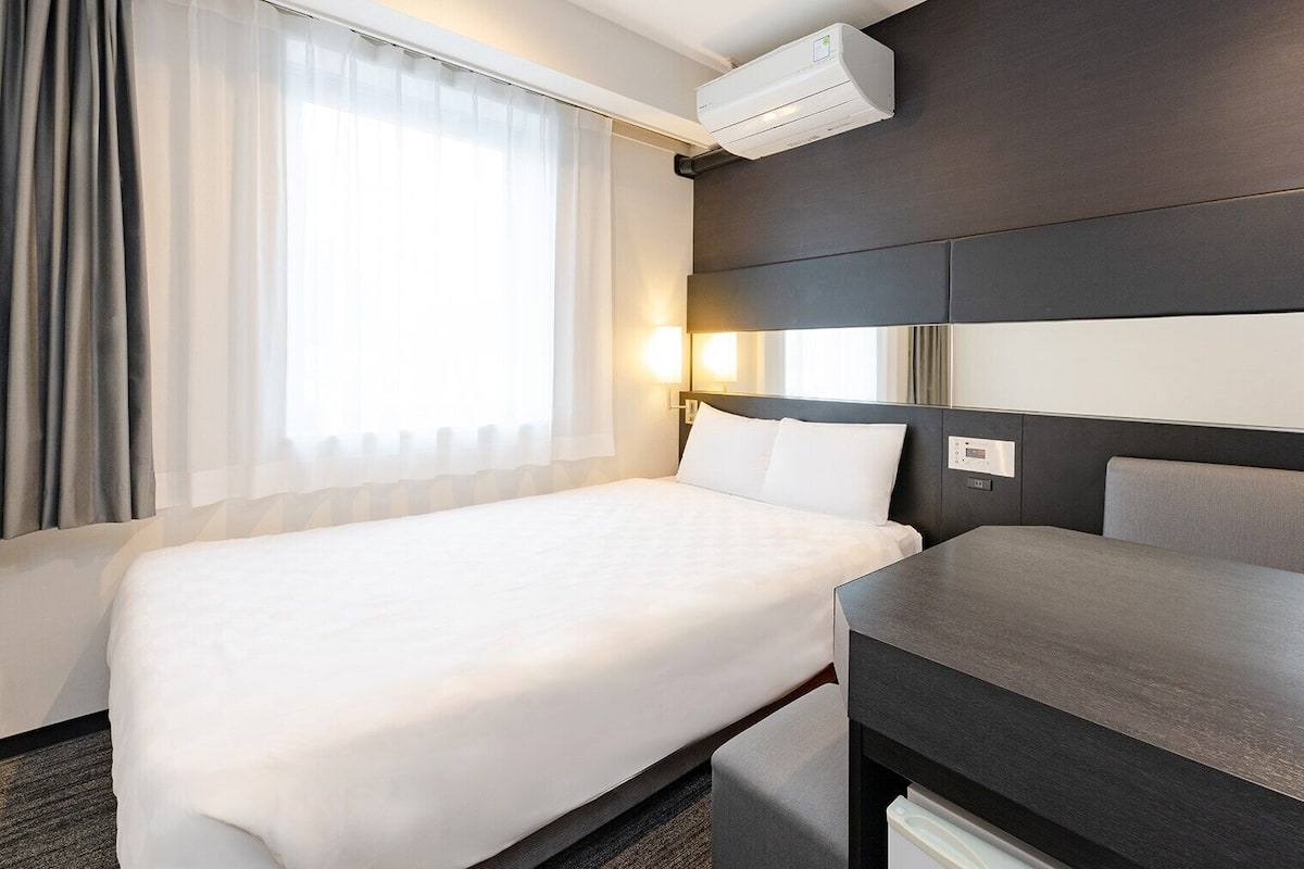 A hotel room with a bed, bedside table, and an air conditioning unit.