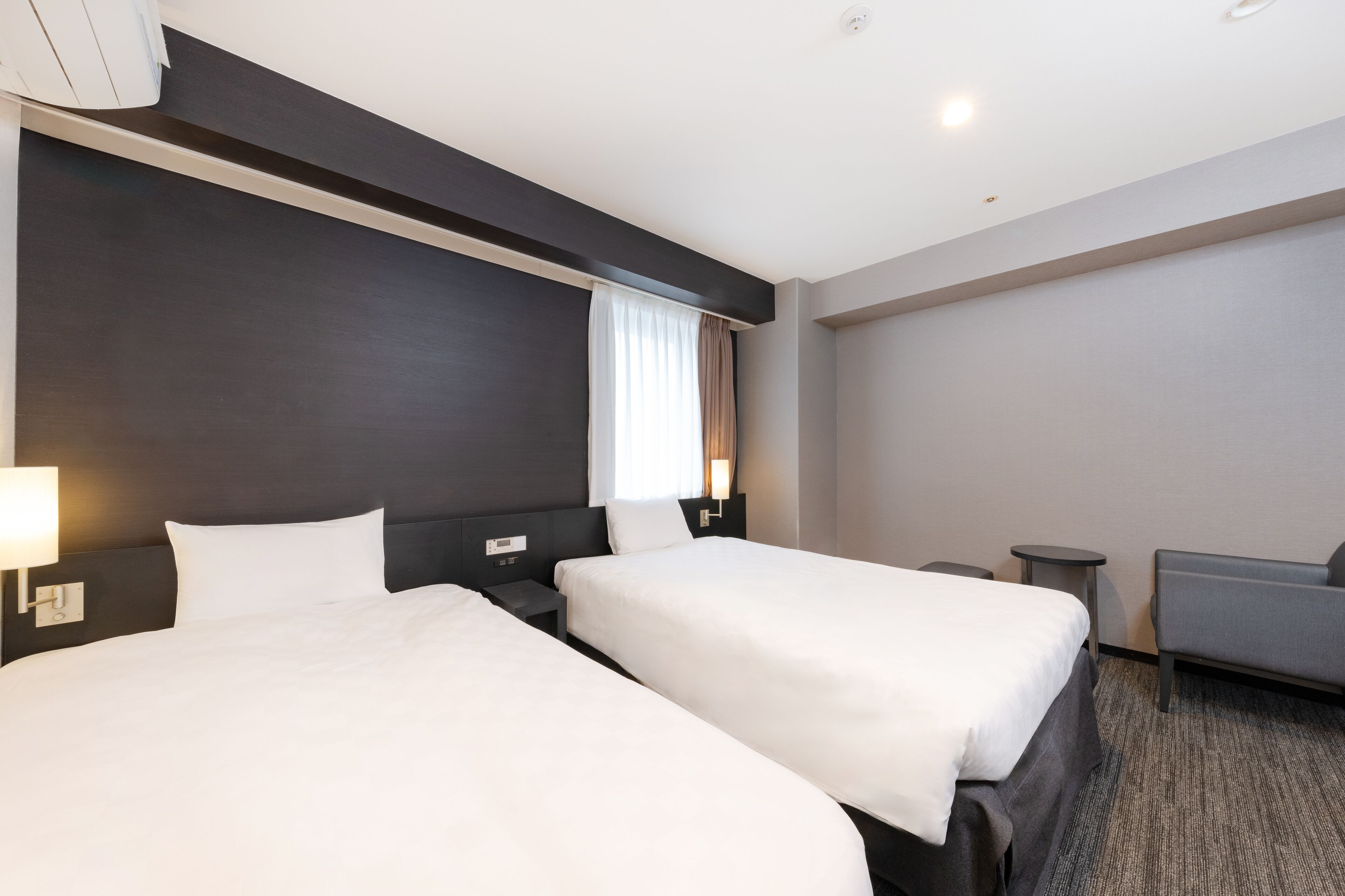 Una habitación de hotel con dos camas, un sofá, una mesita y una lámpara.