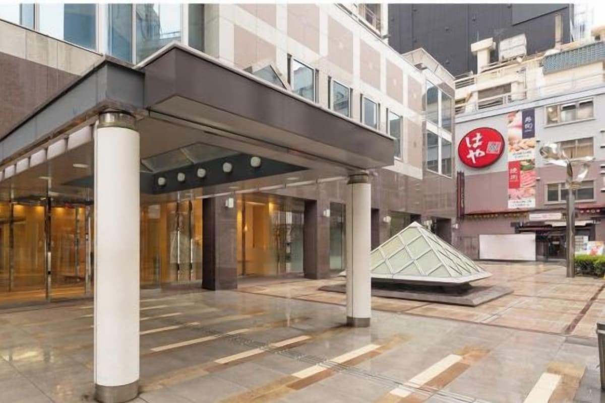 A modern hotel entrance with a glass facade, a covered entrance area, and a distinctive red sign.