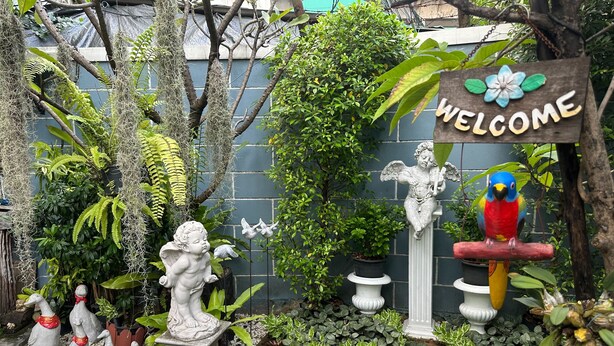 A garden with a welcome sign, various plants, and decorative statues. - BAANFAHSAI ANU (Bangkok)