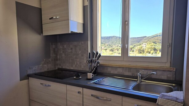 A modern kitchen with a large window, a sink, and wooden cabinets.
