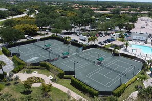 Un gran complejo de canchas de tenis al aire libre, con varias canchas, rodeado de vegetación y una piscina.