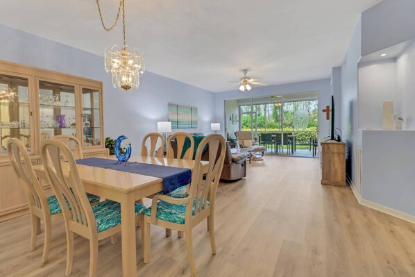 A spacious dining area with a wooden table and chairs, a chandelier, and a view of the outdoors through large sliding glass doors.