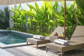 Ein Poolbereich mit Korlounge-Stühlen, Handtüchern und einem Tisch mit Früchten und einem Getränk.