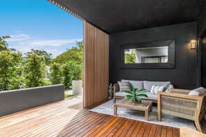 Uma área de estar moderna ao ar livre, com um deck de madeira, um sofá, uma mesa de centro e um espelho na parede.