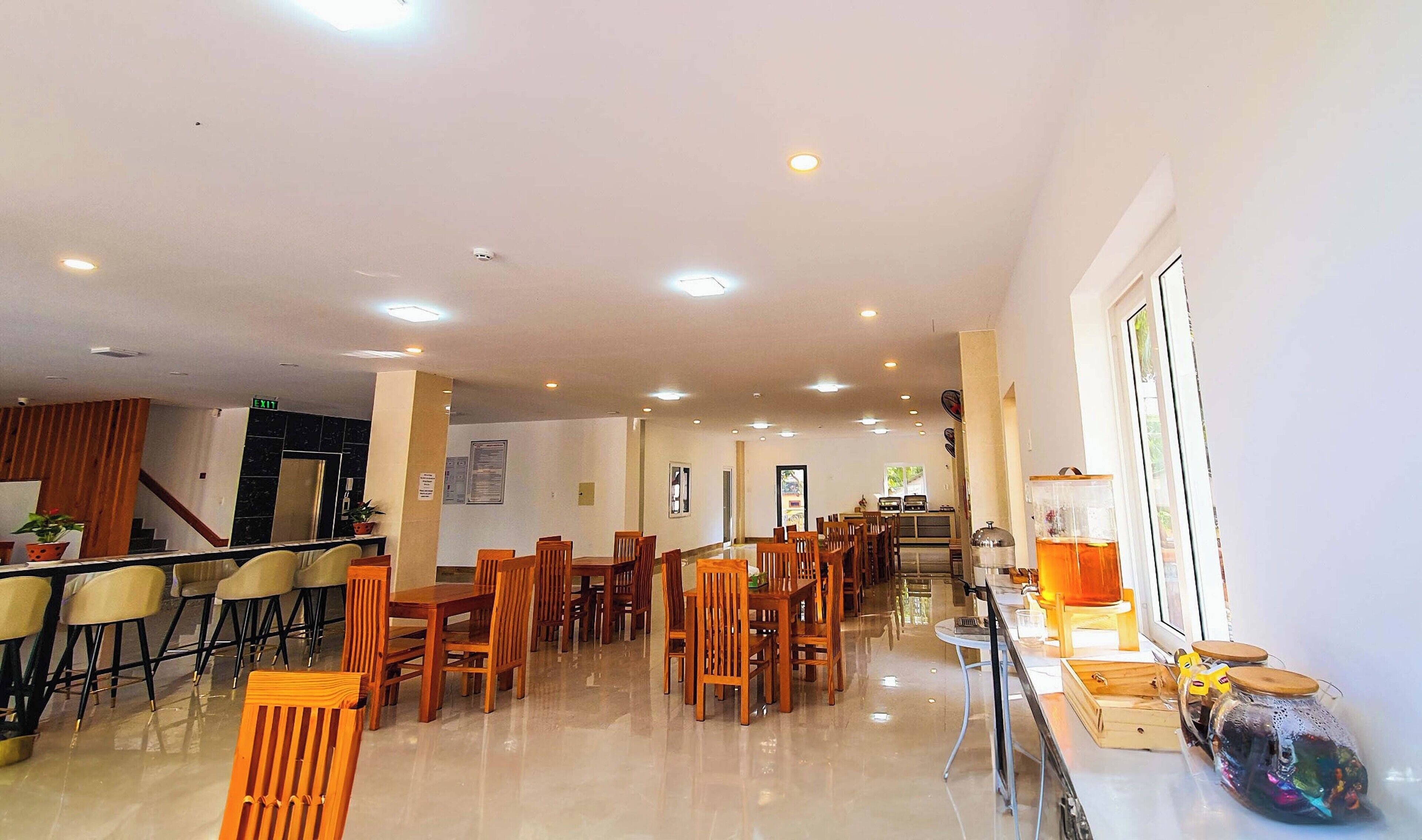 A spacious dining area with multiple wooden tables and chairs, a reception desk, and a clear view of the entrance.