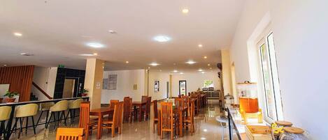 A spacious dining area with multiple wooden tables and chairs, a reception desk, and a clear view of the entrance.