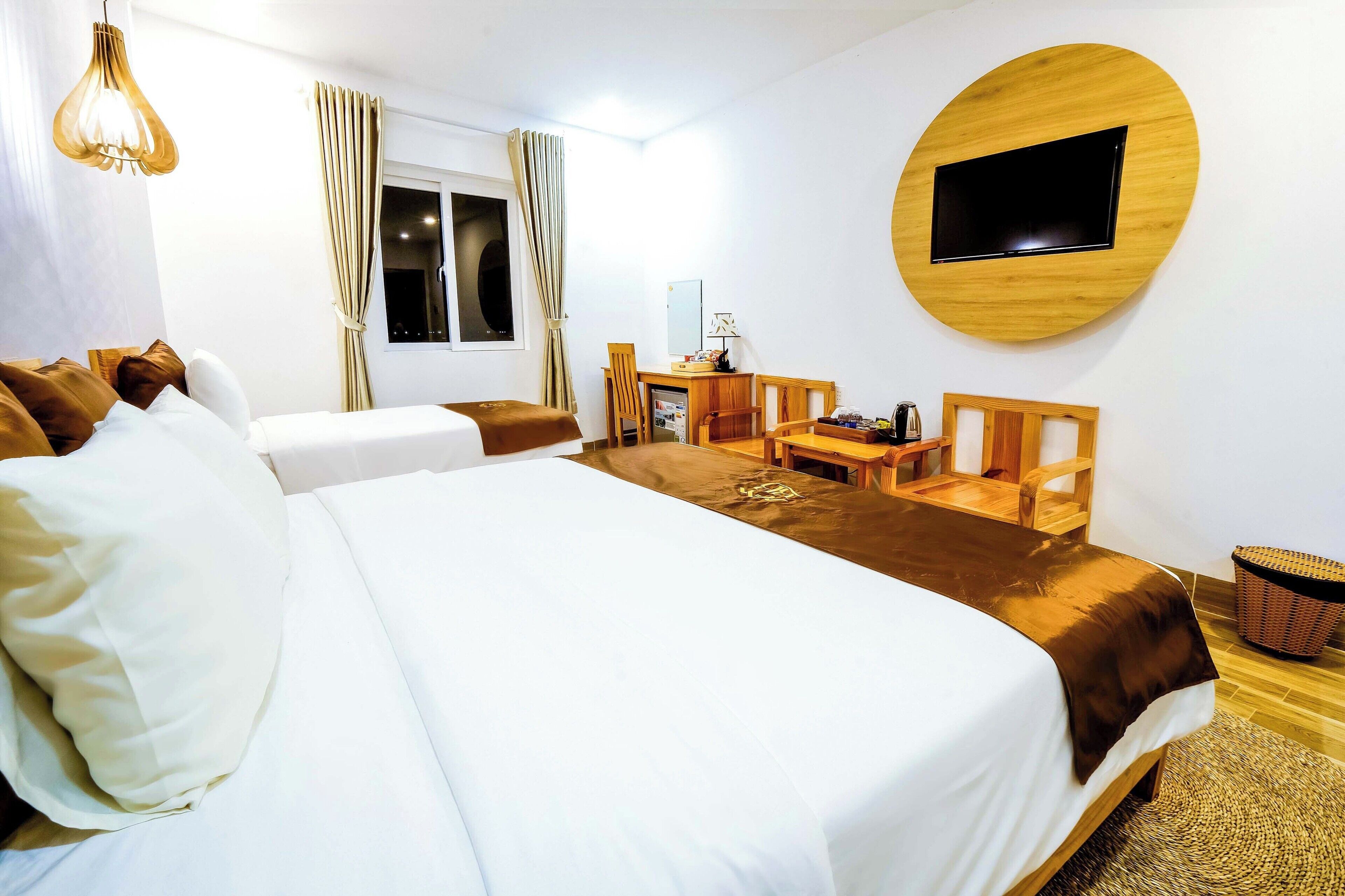 Une chambre d’hôtel avec un grand lit, un bureau, une chaise, un téléviseur fixé au mur et une fenêtre avec des rideaux.