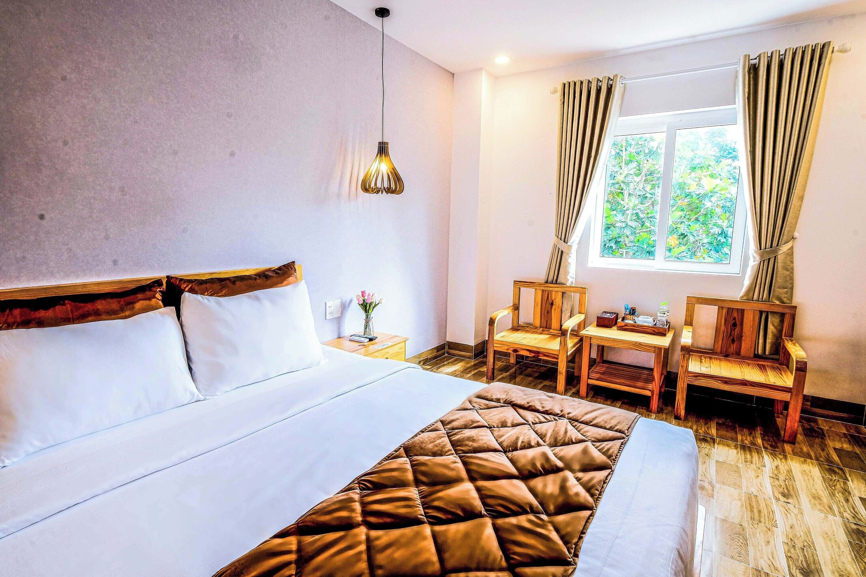 A hotel room with a large bed, a wooden desk, two chairs, and a window with curtains.