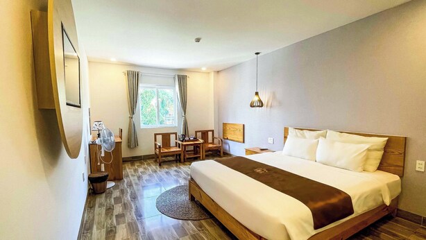 A hotel room with a large bed, a desk with a chair, a small table, a lamp, and a window with curtains.