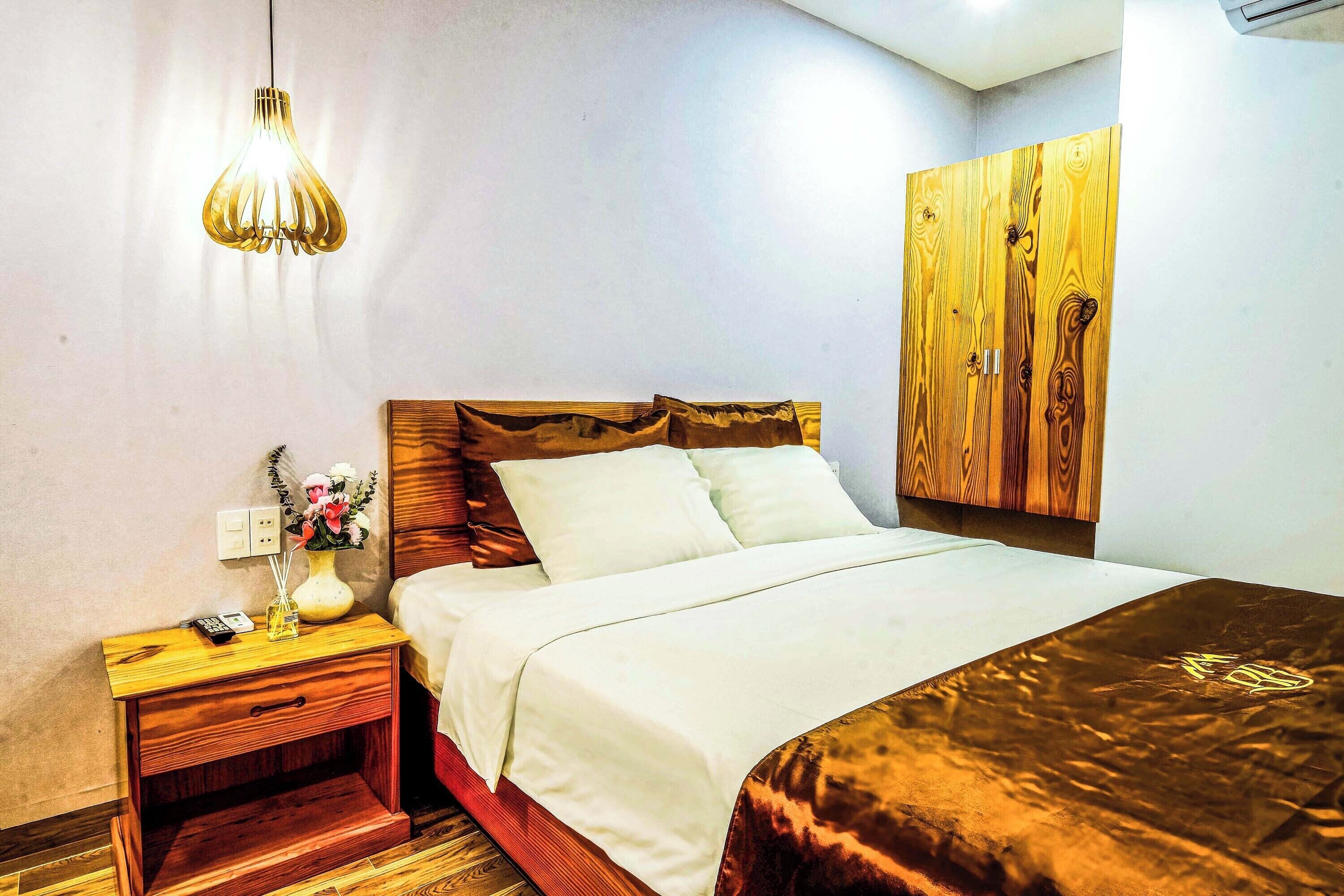A bedroom with a wooden headboard, a bedside table with a lamp, and a bed with white bedding.