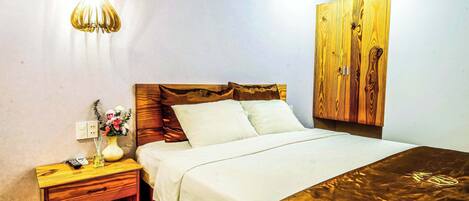 A bedroom with a wooden headboard, a bedside table with a lamp, and a bed with white bedding.