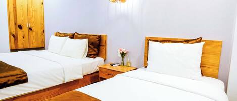 A hotel room with two beds, wooden headboards, white bedding, a nightstand with a vase of flowers, and a hanging light fixture.