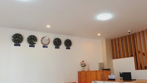 A reception area with a wooden reception desk, a vase with flowers, and five clocks labeled with city names.