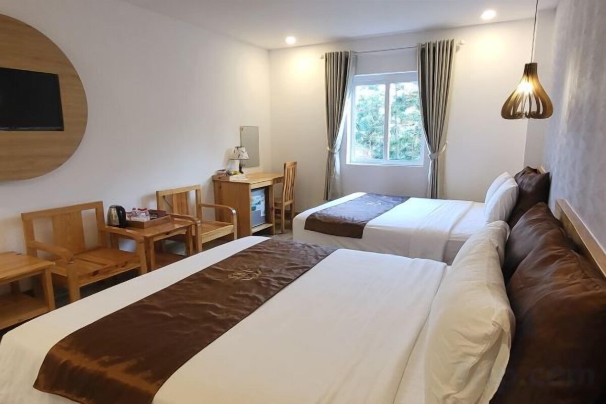 Habitación de hotel con dos camas, un escritorio, una silla y un televisor montado en la pared.