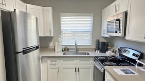 A compact kitchen with white cabinets, a stainless steel refrigerator, a stove, and a microwave.
